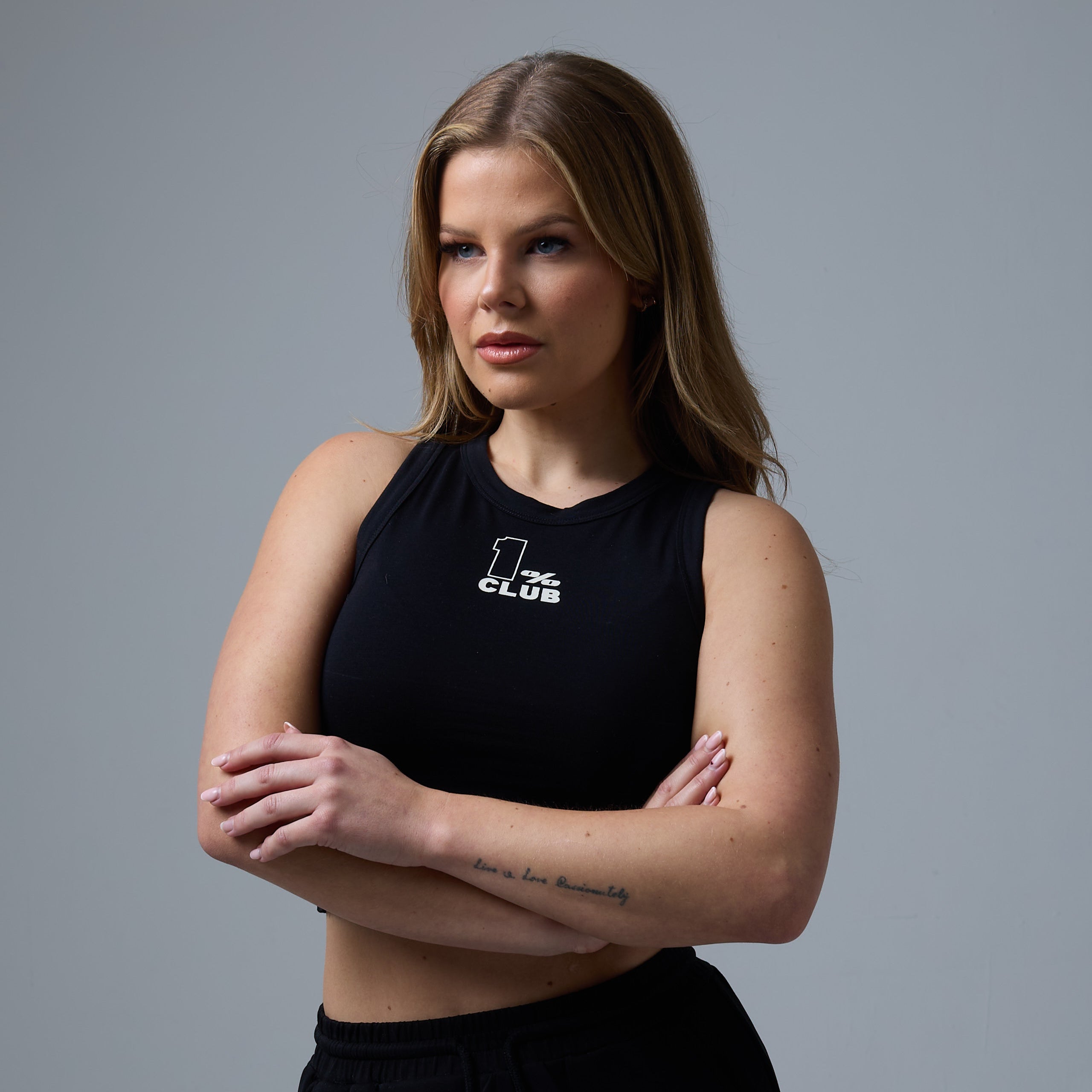 Model wearing a sleek black crop tank top from The 1% Club clothing brand, featuring the bold '1% Club' logo on the chest. The design exudes confidence and exclusivity, embodying the brand's modern and empowering aesthetic.